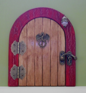 brown wooden handcrafted faerie door with dragon charm and red frame