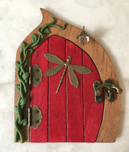 red handcrafted faerie door with dragonfly and vine on left side of brown frame