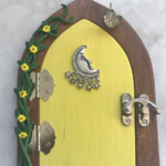 pastel yellow handcrafted faerie door with moon charm and vine on brown frame