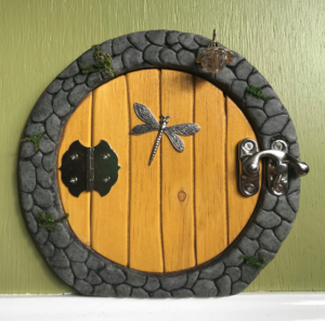 yellow hobbit shaped handcrafted faerie door with dragonfly and stone frame