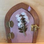 light purple handcrafted faerie door with flowers and a brown frame