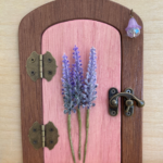 pink handcrafted faerie door with purple flowers and brown frame