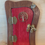 red handcrafted faerie door with a tree charm and brown frame